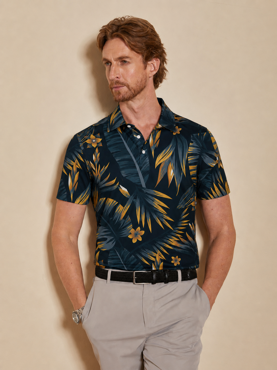 Man wearing a navy blue tropical floral print golf polo and grey trousers.