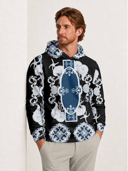 Man wearing a black hoodie with a blue and white ornate nautical print and khaki pants.