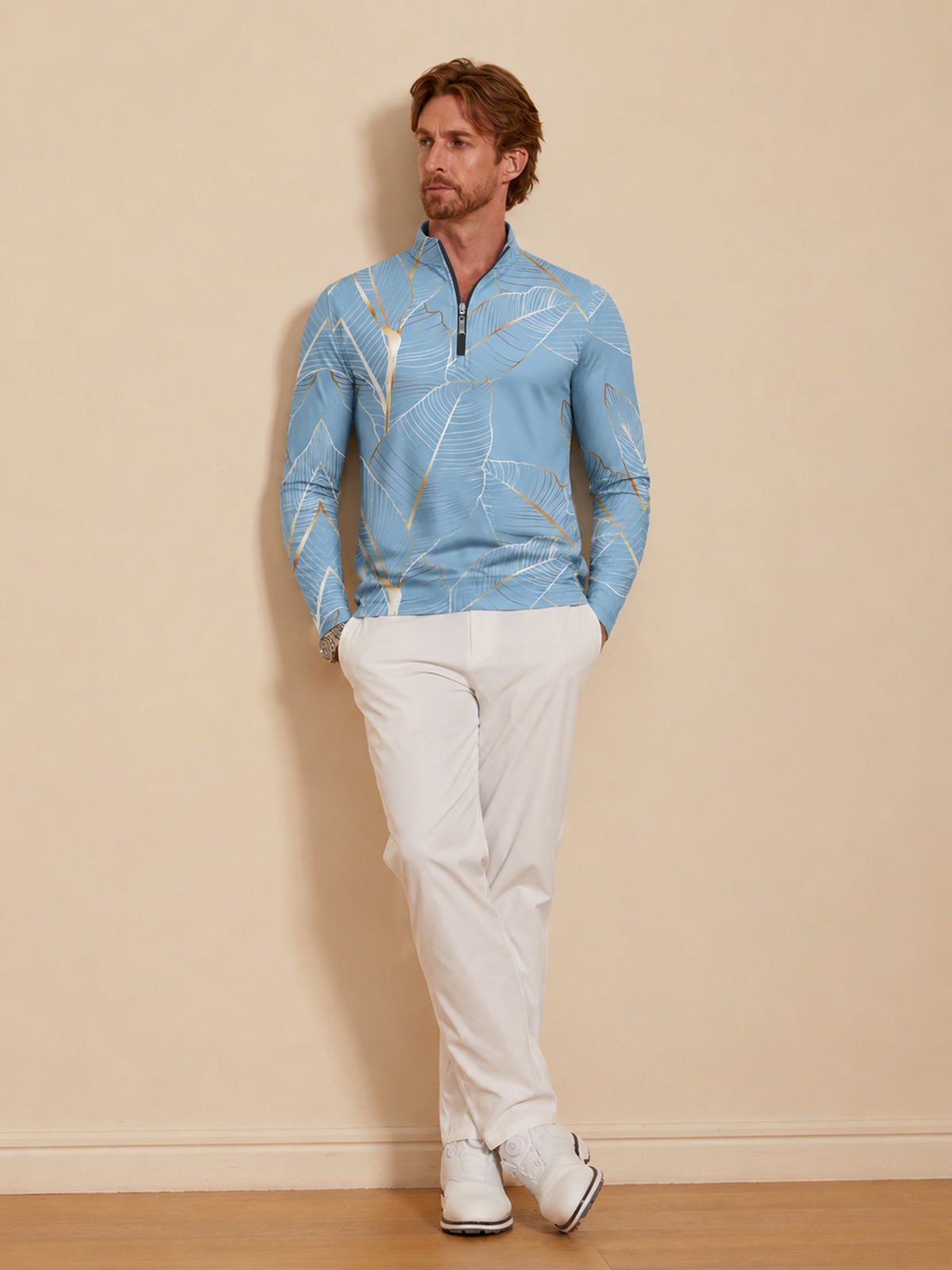 Man wearing a light blue quarter-zip golf shirt with gold leaf print and white golf pants.