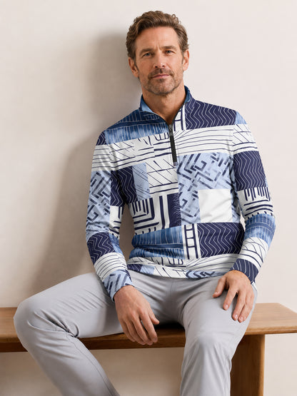 Man wearing a blue and white geometric print quarter-zip golf shirt and grey pants.