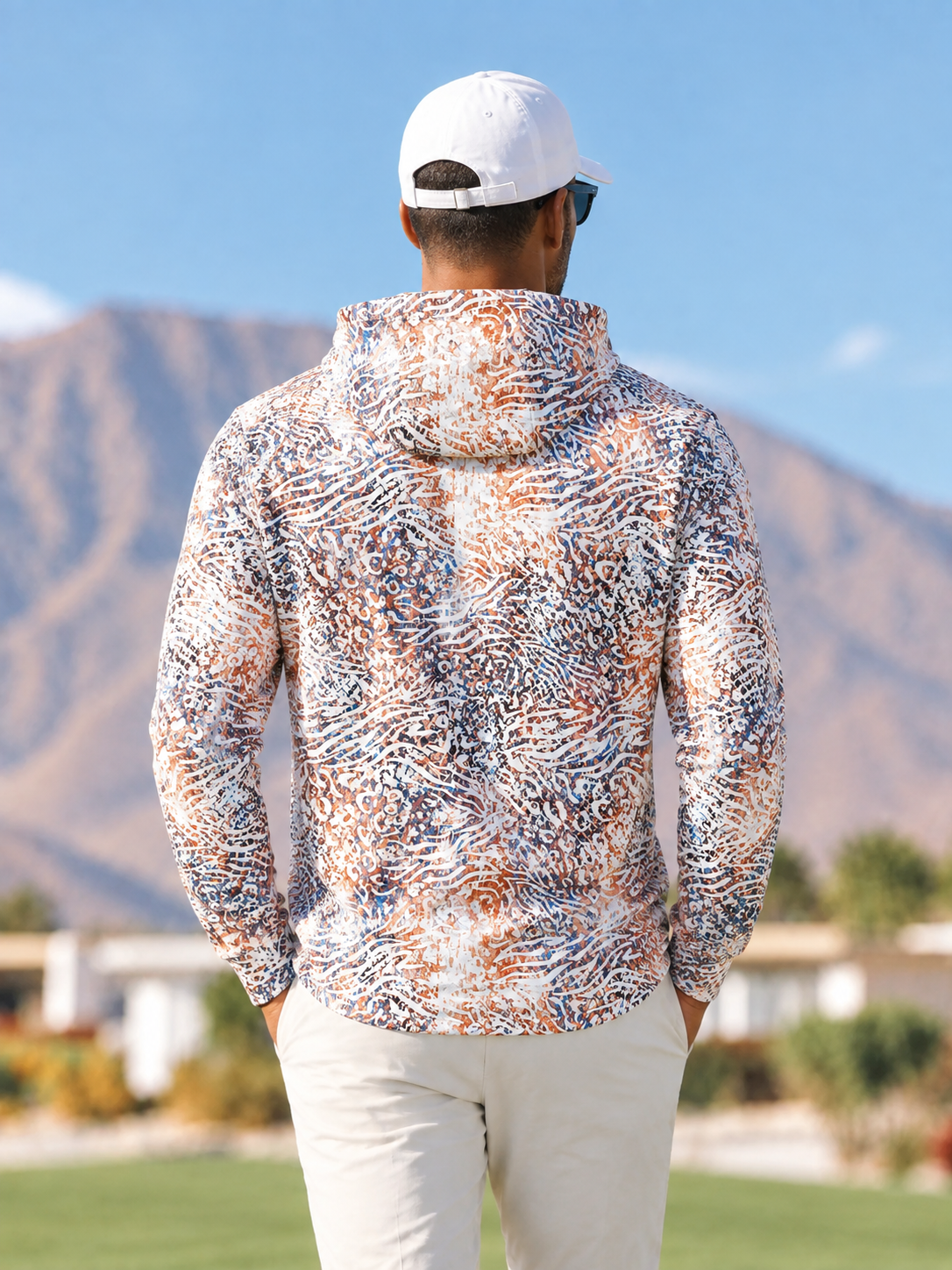 Man wearing a hooded performance golf shirt with an abstract animal print and white cap.