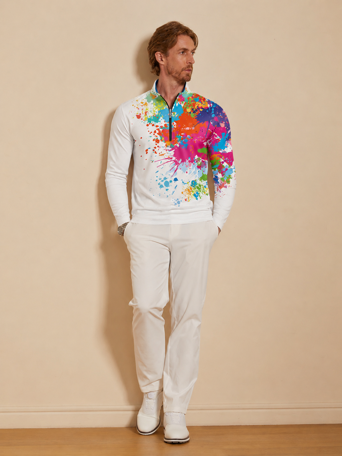 Man wearing a white quarter-zip golf pullover with a colorful paint splatter print and white pants.