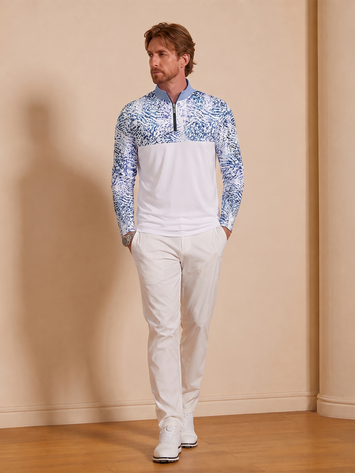 Man wearing a blue and white printed quarter-zip golf shirt and white golf pants.