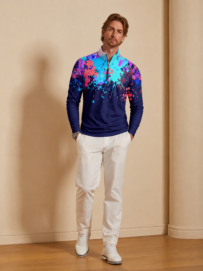 Man wearing a navy blue quarter-zip golf pullover with a colorful paint splatter design and white pants.