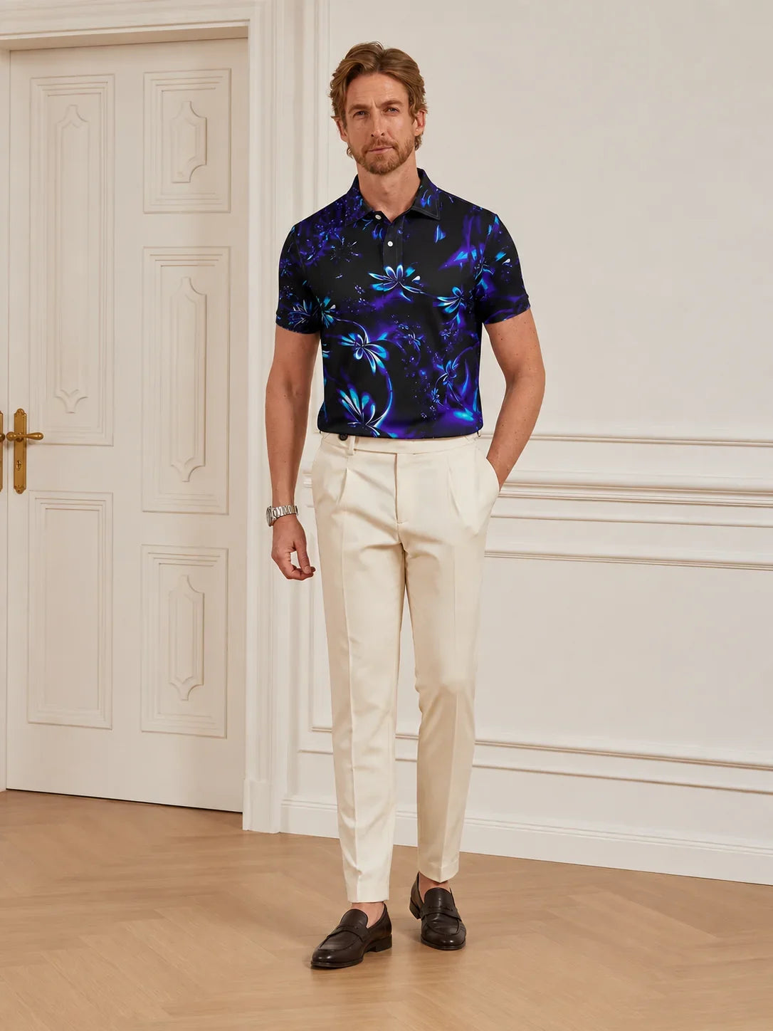 Man wearing a navy blue floral print performance golf polo and white trousers.